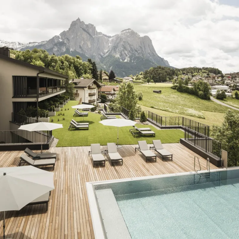 Vista estiva dell'Hotel Alpenflora con piscina nel giardino e vista sullo Sciliar