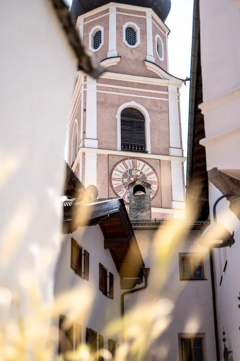 Campanile barocco di Castelrotto incorniciato da erbe autunnali nella luce del sole