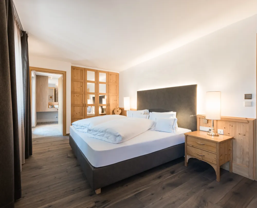 Doppelzimmer Classic im Wellnesshotel Alpenflora mit Doppelbett, Holzschrank mit Glastüren und Durchgang zum Badezimmer.