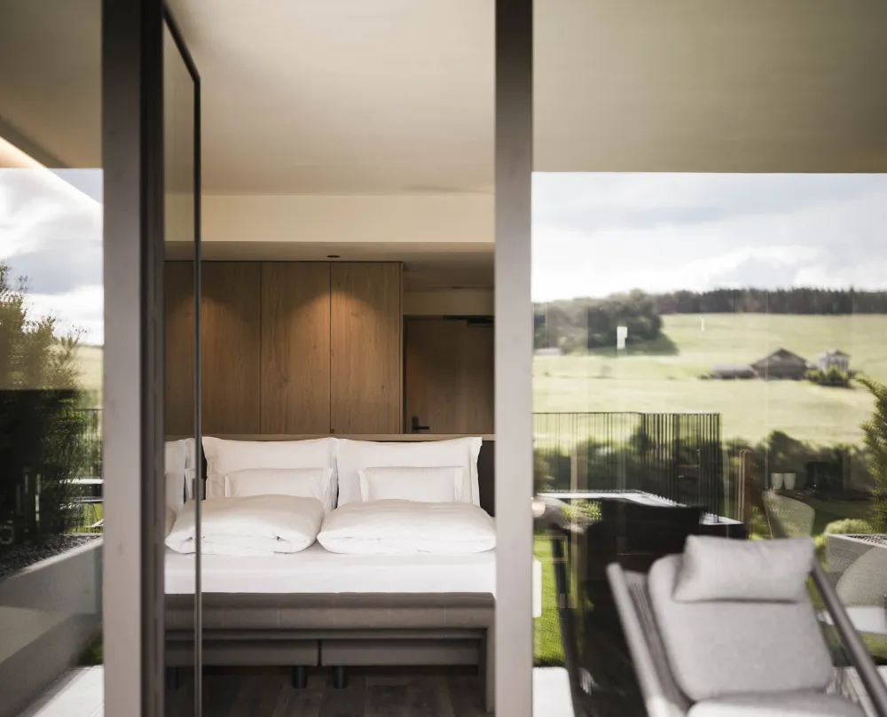 Blick von der Terrasse durch die offene Glastür ins Zimmer Garden Relax mit grüner Wiese im Hintergrund im Wellnesshotel Alpenflora.