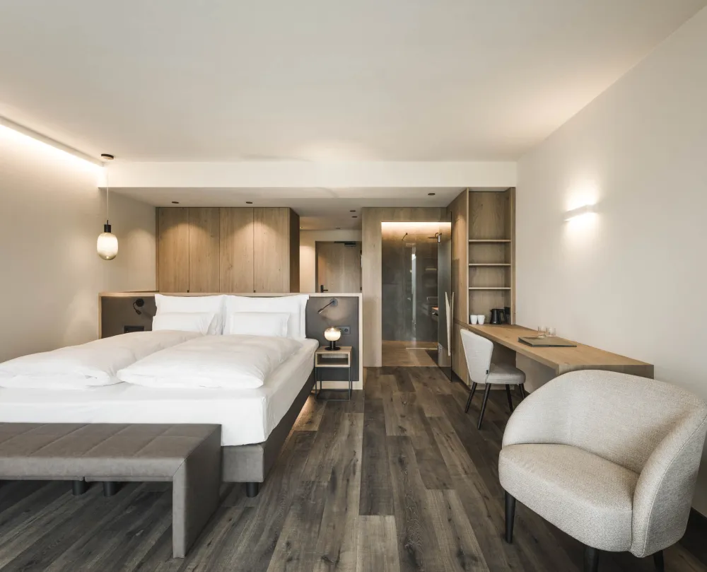 Doppelzimmer Garden View im Wellnesshotel Alpenflora mit Doppelbett, Schreibtisch, Sessel und einsehbarer Dusche.