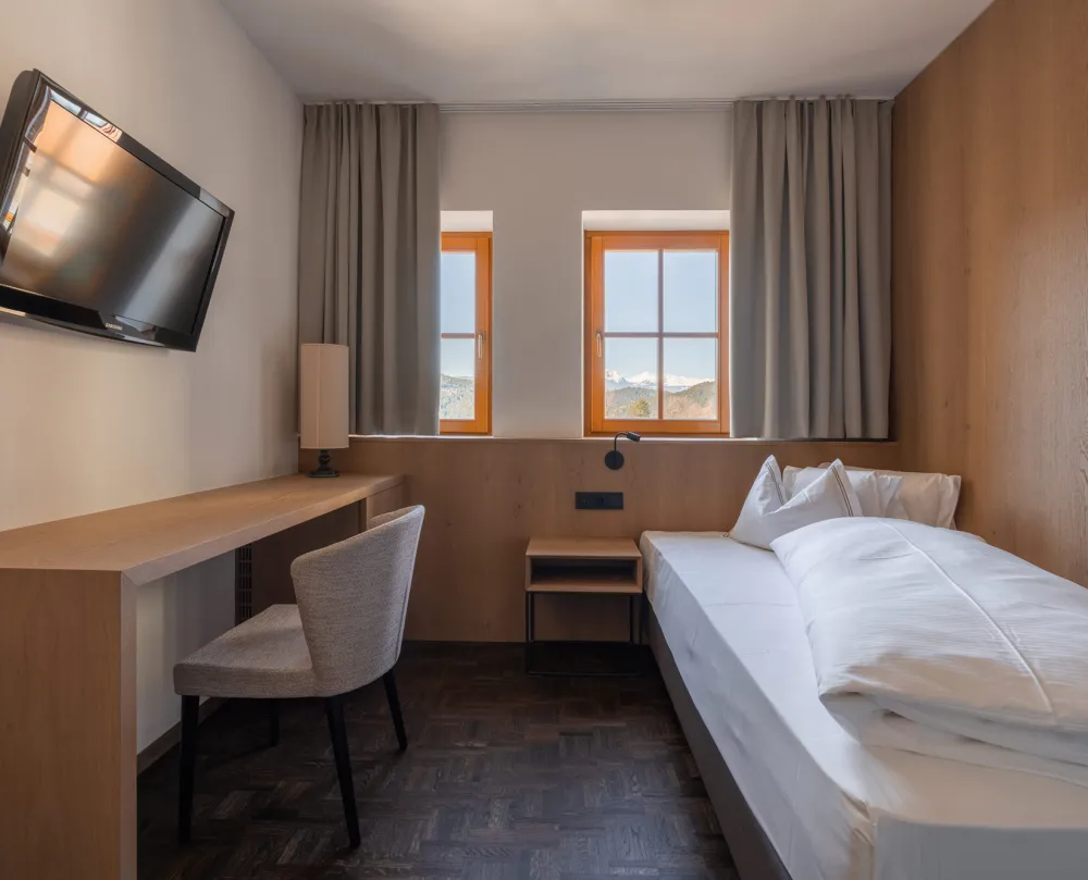 Einzelzimmer Single Stay im Wellnesshotel Alpenflora mit Bett, Schreibtisch, Fernseher und Fenstern mit Bergblick.