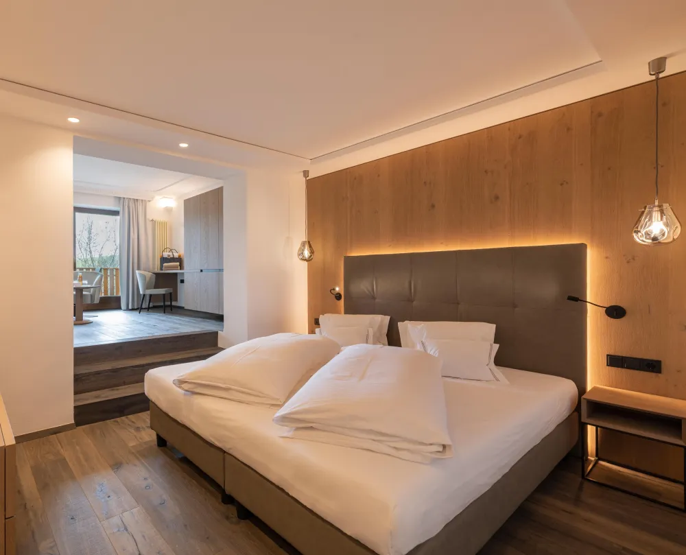 Schlafbereich der Sun Suite im Wellnesshotel Alpenflora mit Doppelbett, Holzwandverkleidung und Durchgang zum Wohnraum.